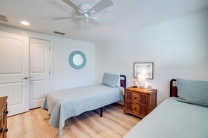 A bedroom with two single beds, a ceiling fan, a bedside table with a lamp, and a wall clock.