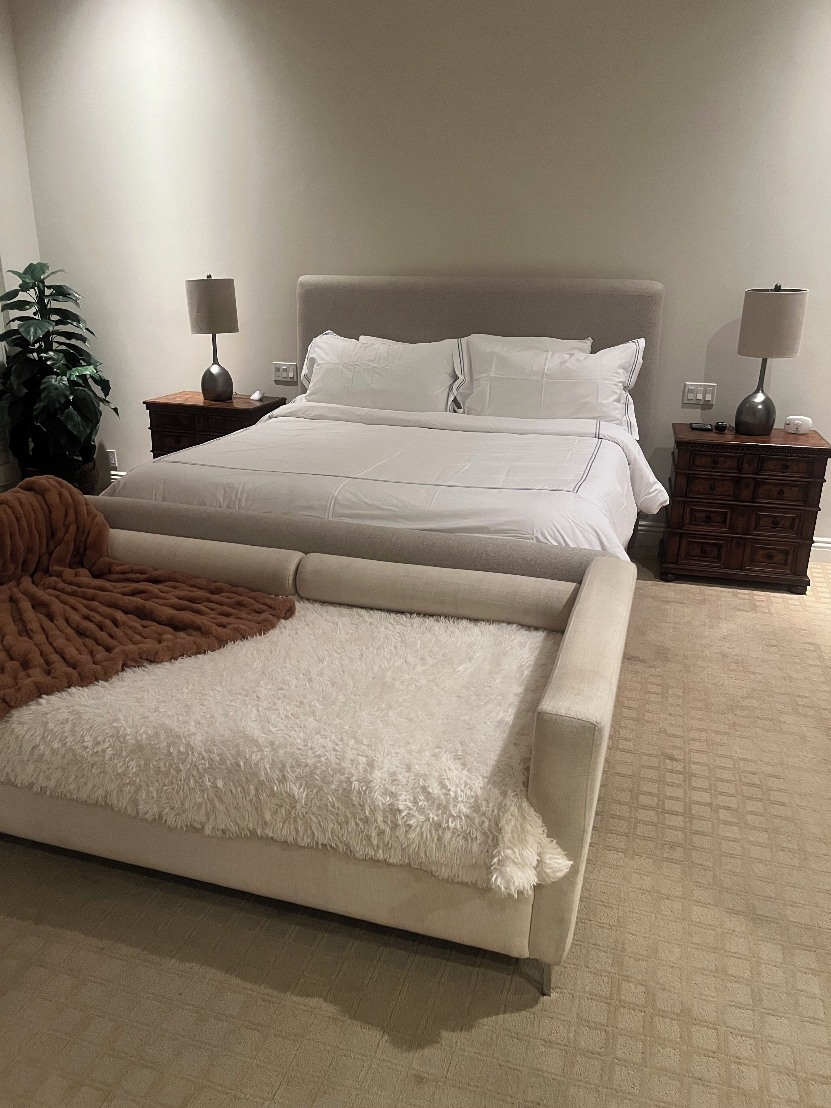 Une chambre à coucher avec un lit, des tables de chevet, une lampe, une plante et un canapé.