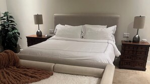 A bedroom with a bed, nightstands, a lamp, a plant, and a sofa. - Elegant Private 2-Bedroom Ensuite Condo with Expansive Living and Dining Areas (Rancho Mirage)
