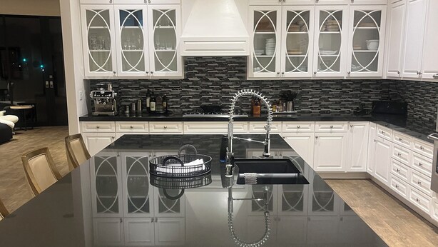 A modern kitchen with white cabinetry, a black countertop, and a central island. - Elegant Private 2-Bedroom Ensuite Condo with Expansive Living and Dining Areas (Rancho Mirage)