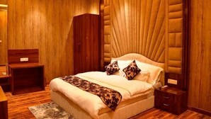 A bedroom with a large bed, wooden panel walls, a headboard, and a bedside table. - Hotel Blue Stone (Kanpur)