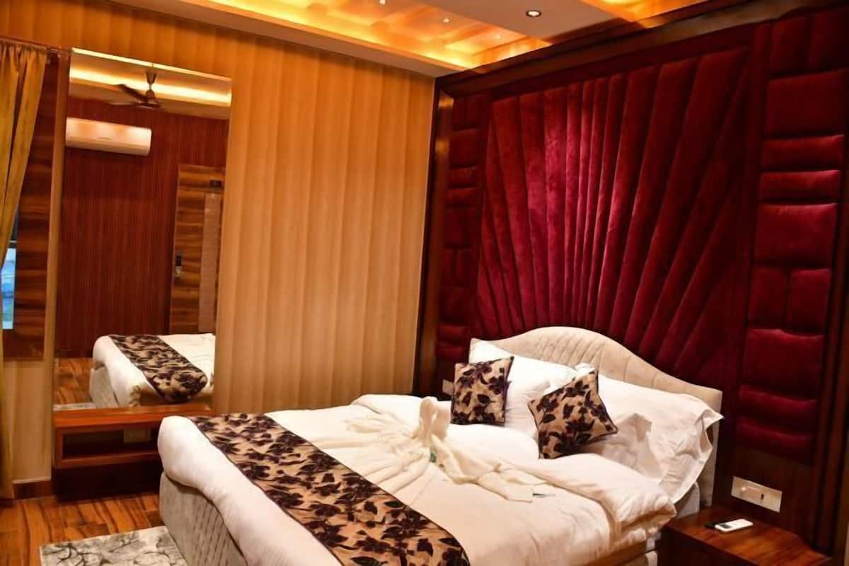 A hotel room with a bed, a mirror, a red velvet headboard, and a wooden floor.