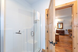 Une salle de bain moderne dotée d’une douche à parois de verre et d’une porte en bois donnant sur un espace de vie comprenant un canapé et une table basse.