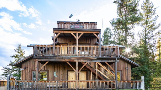 A rustic wooden cabin with a balcony, a staircase, and a solar panel on the roof. - Epic Group Stay | 3 Cabins w/ Views | Near Glacier NP, Skiing & Summer Adventures! (Columbia Falls)