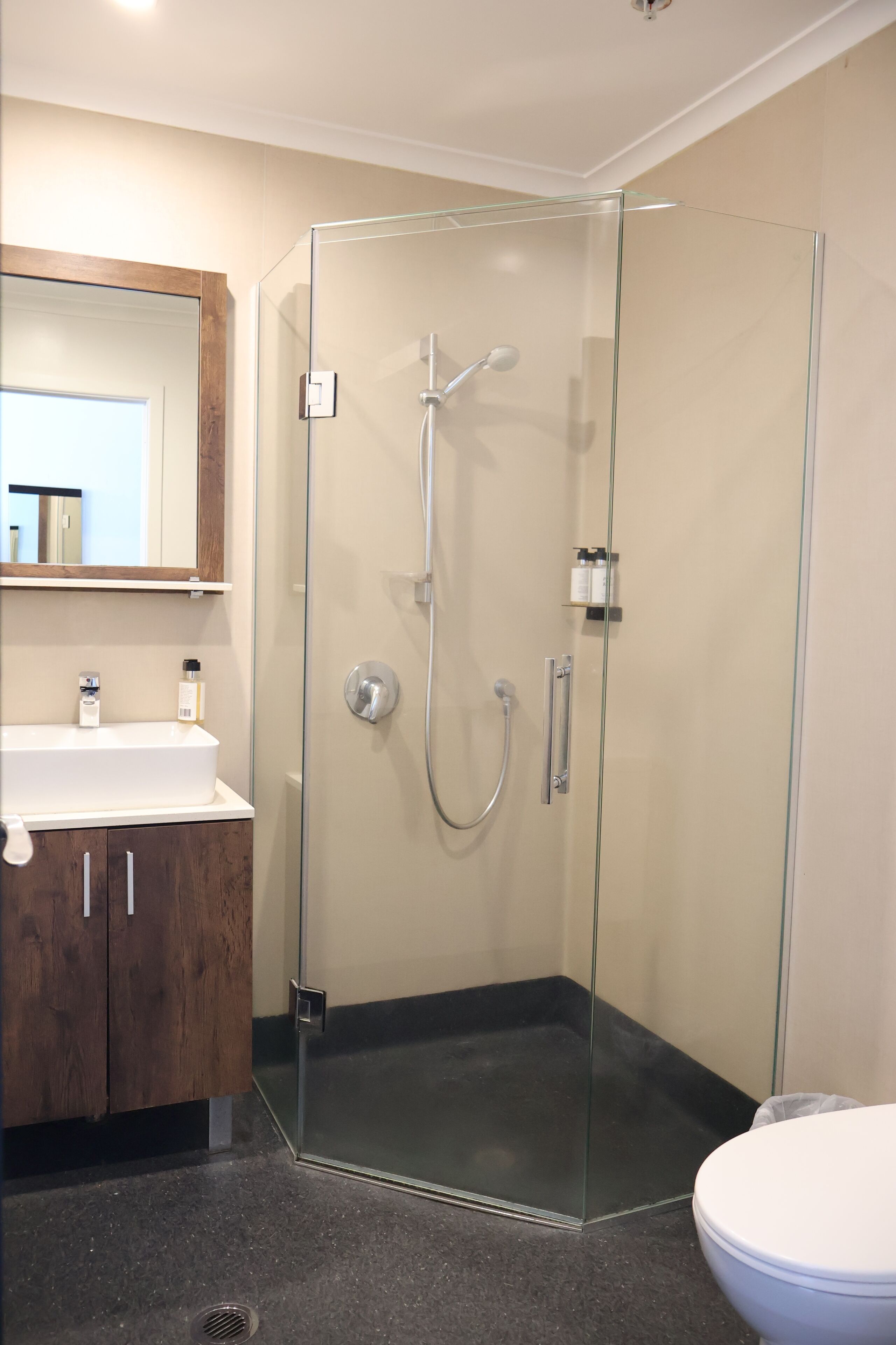 A bathroom with a glass-enclosed shower, a white sink, and a wooden cabinet.