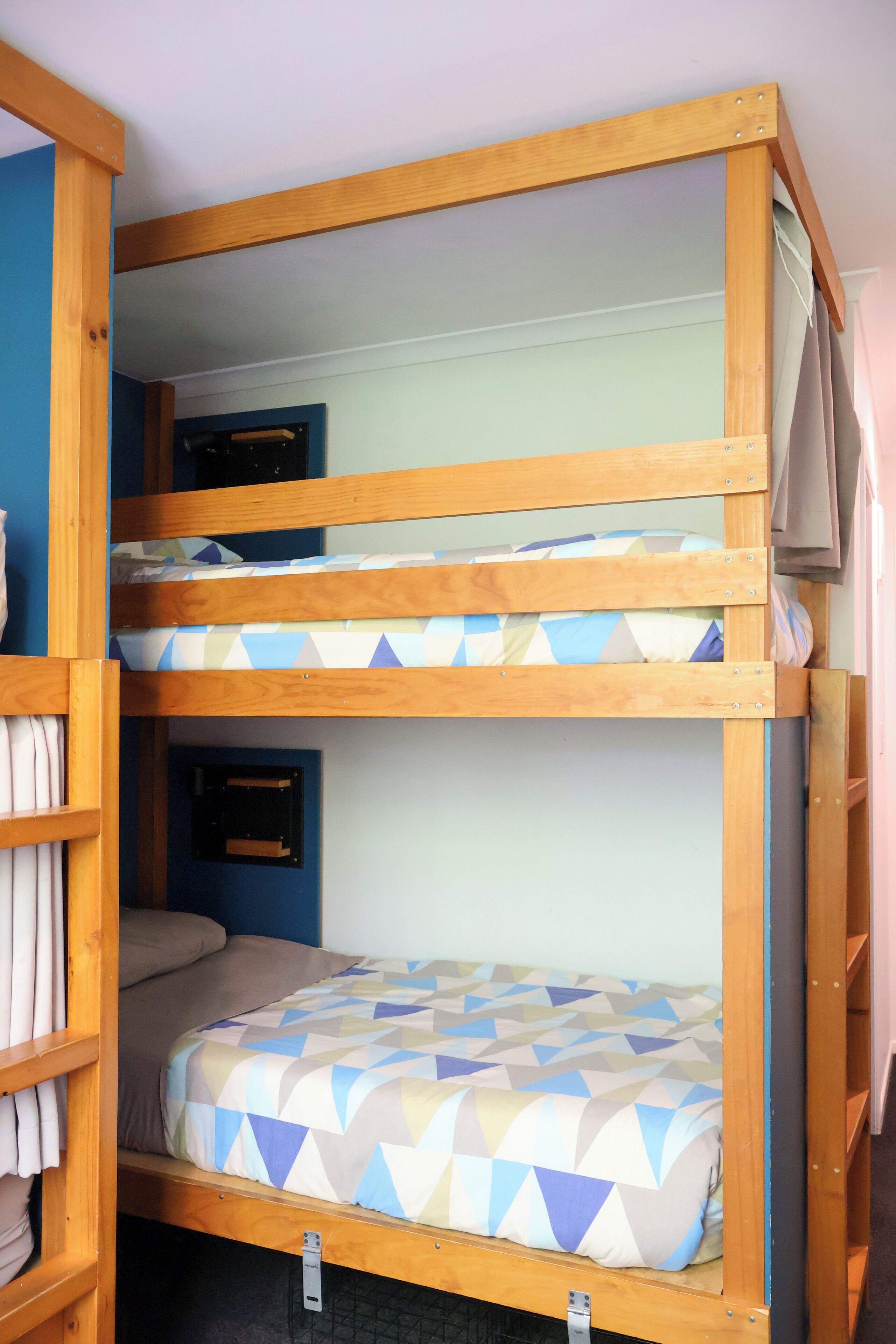 A bunk bed with a geometric patterned bedspread, a wooden frame, and a shelf unit with folded items.