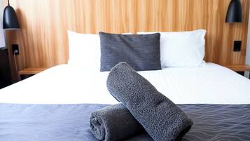 Ein ordentlich bezogenes Bett mit grauer Decke und Kissen, einem Holz-Kopfteil und zwei schwarzen Pendelleuchten.
