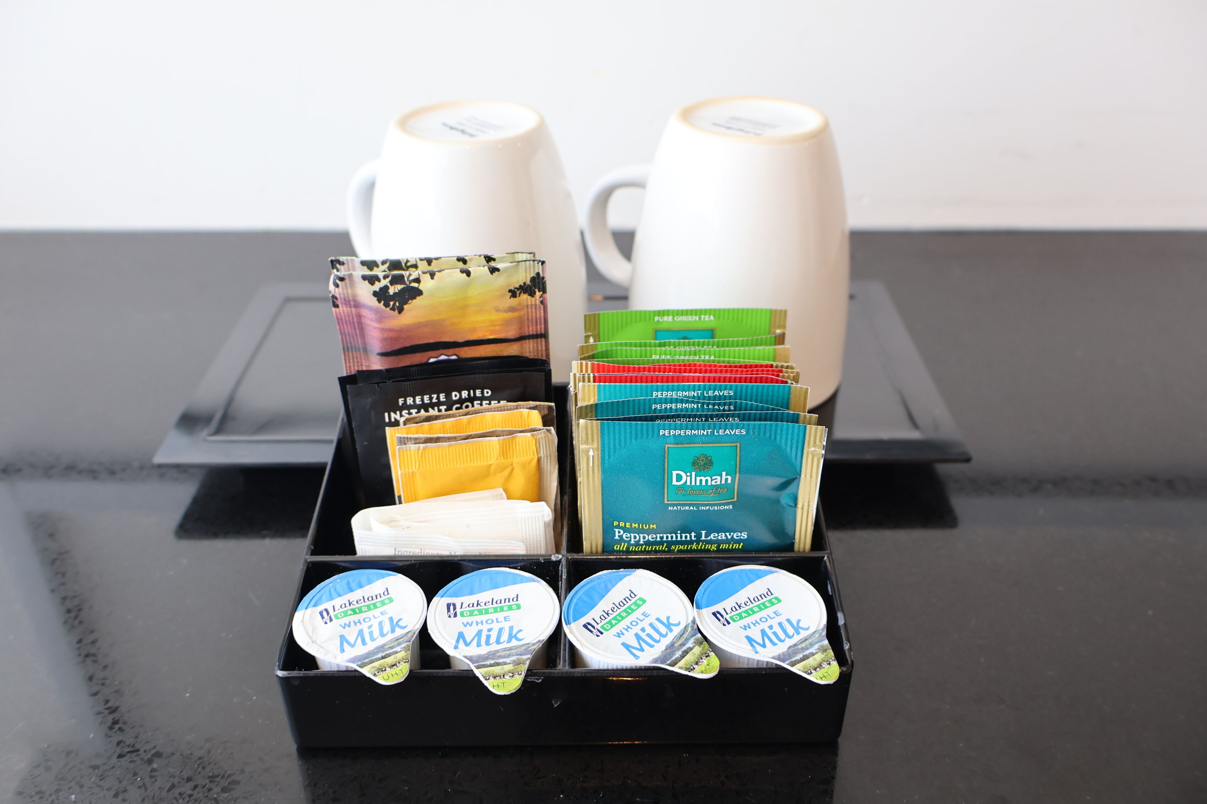 A coffee and tea station with a variety of products including whole milk, instant coffee, and Dilmah premium peppermint leaves.
