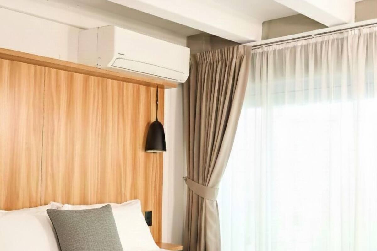 Ein Hotelzimmer mit einem Bett, einem Holzkopfteil, einer schwarzen Pendelleuchte und einem Fenster mit Vorhängen.