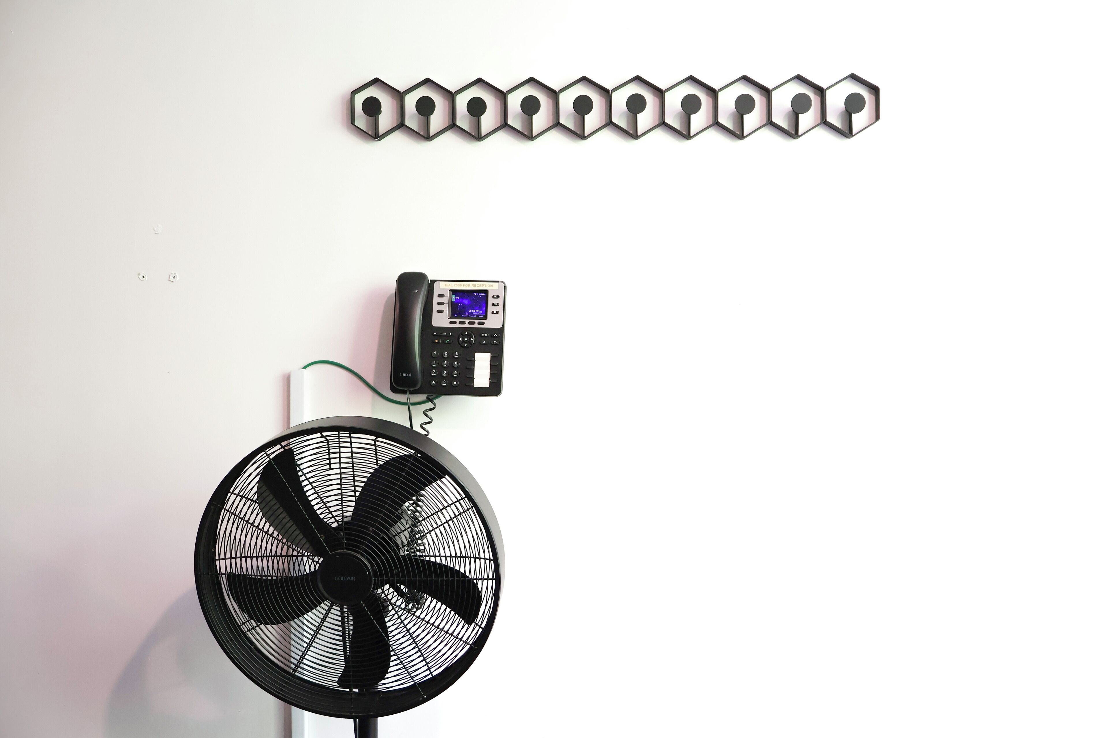 A room with a white wall, a black fan, and a wall-mounted telephone.