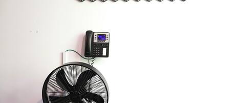 A room with a white wall, a black fan, and a wall-mounted telephone.