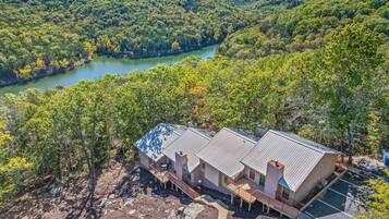 A cabin with a metal roof, surrounded by dense forest and a river.