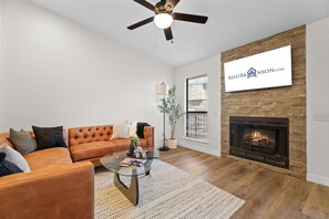 A living room with a leather sofa, a glass coffee table, a fireplace, and a ceiling fan.