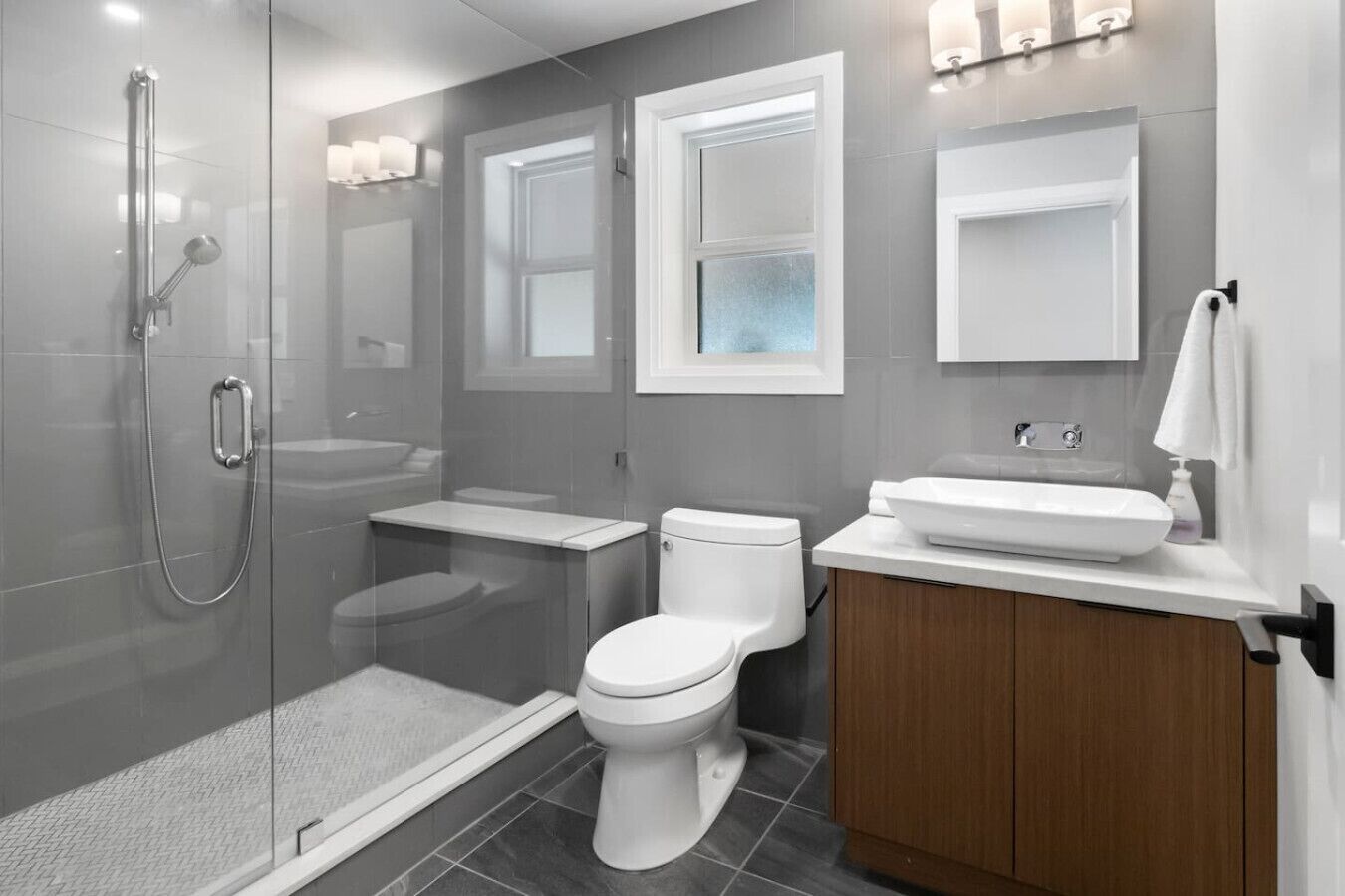 Un baño moderno con ducha de vidrio, inodoro, lavamanos y tocador con espejo.
