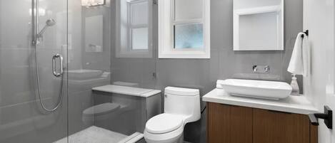 Un baño moderno con ducha de vidrio, inodoro, lavamanos y tocador con espejo.