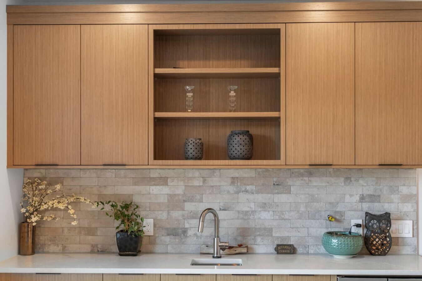 Een keuken met houten kastjes, een betegelde spatwand, een spoelbak en decoratieve objecten.