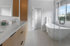 Un baño moderno con una bañera independiente, un espejo grande y una encimera con artículos de aseo.