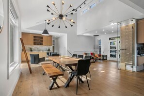 Una cocina moderna con armarios de madera, un comedor con mesa y bancos de madera, y una lámpara de araña grande.