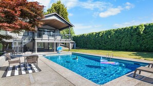 Een modern huis met een zwembad, tuinmeubilair en een verzorgde tuin.