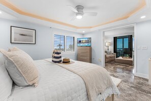 Ein Schlafzimmer mit Bett, Deckenventilator, gerahmtem Bild, Fernseher und Blick ins Freie.
