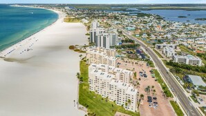 An aerial view of a coastal city with a long sandy beach, high-rise buildings, and a clear blue sky. - Beachside Bliss with Stunning Gulf Views & Resort Amenities – Lander's Sunset Lagoon - Roelens (Fort Myers Beach)
