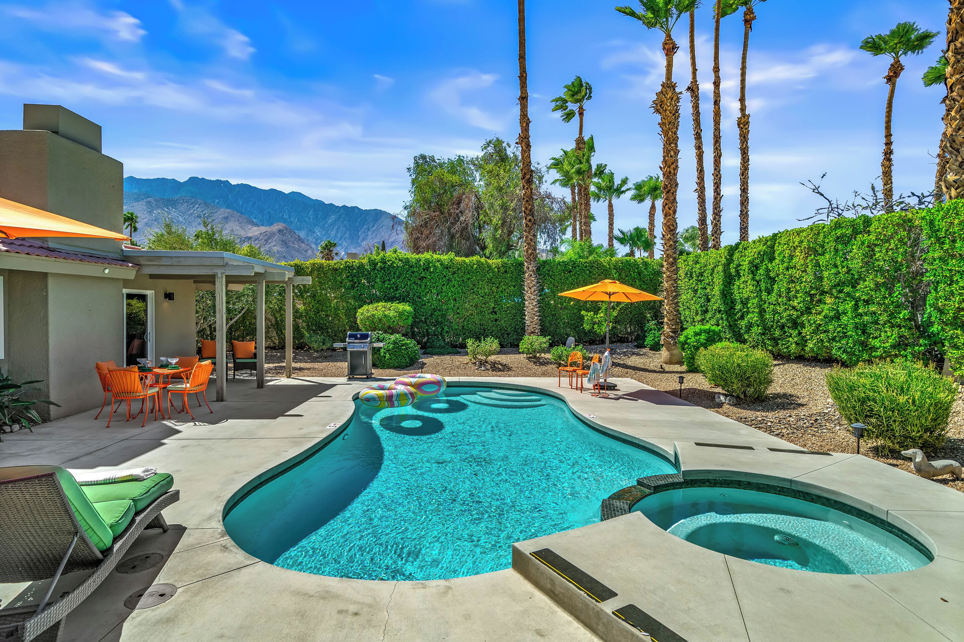 A swimming pool with a hot tub, surrounded by palm trees and a mountain view.
