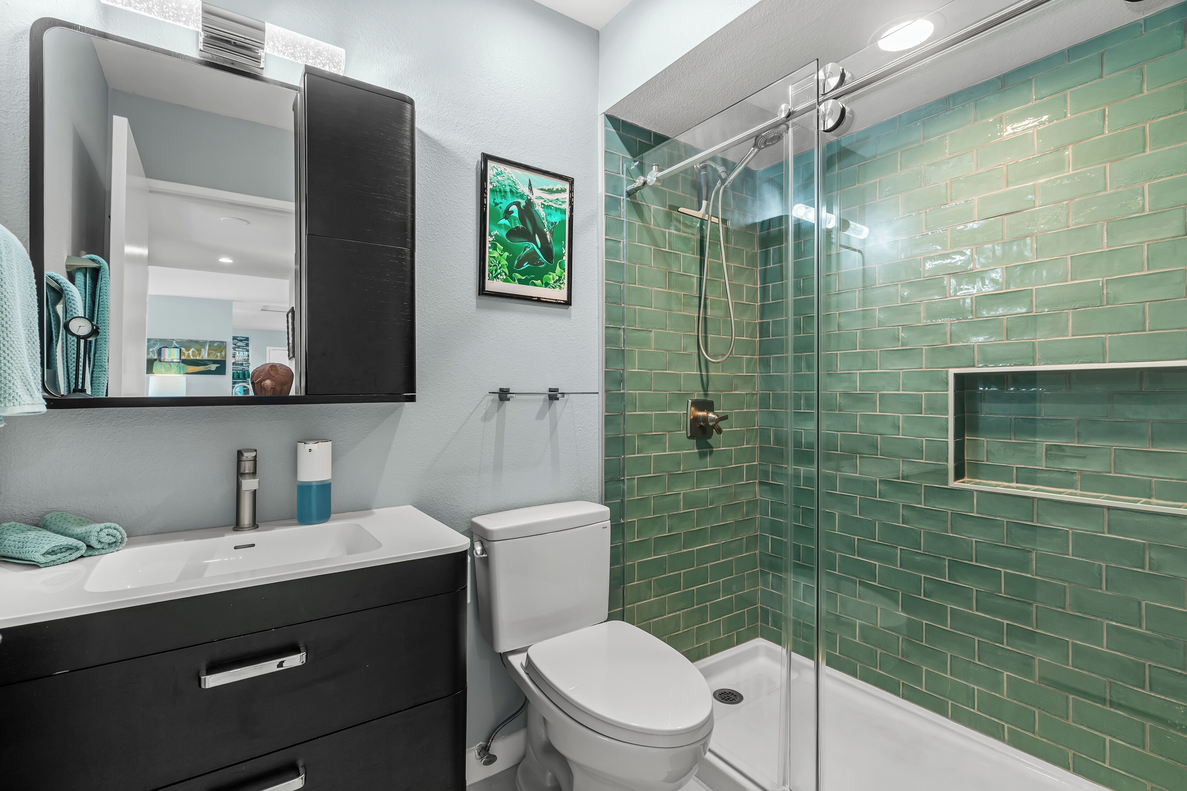 A bathroom with a white sink, a toilet, a glass shower enclosure, and a green-tiled wall.
