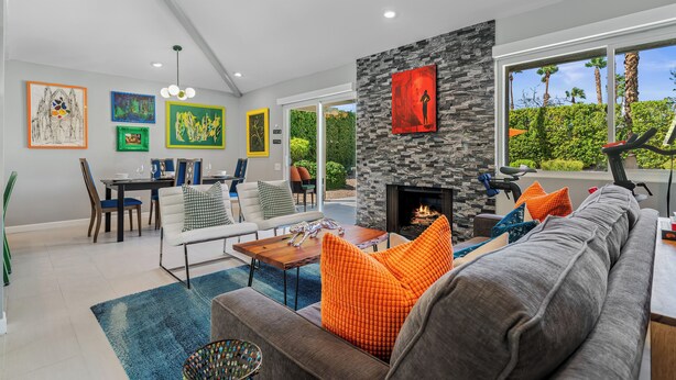 A modern living room with a stone fireplace, a dining area, and artwork on the walls. - Desert Gem - Bold Design, Poolside Fun, Spa, BBQ & Views (Palm Springs)