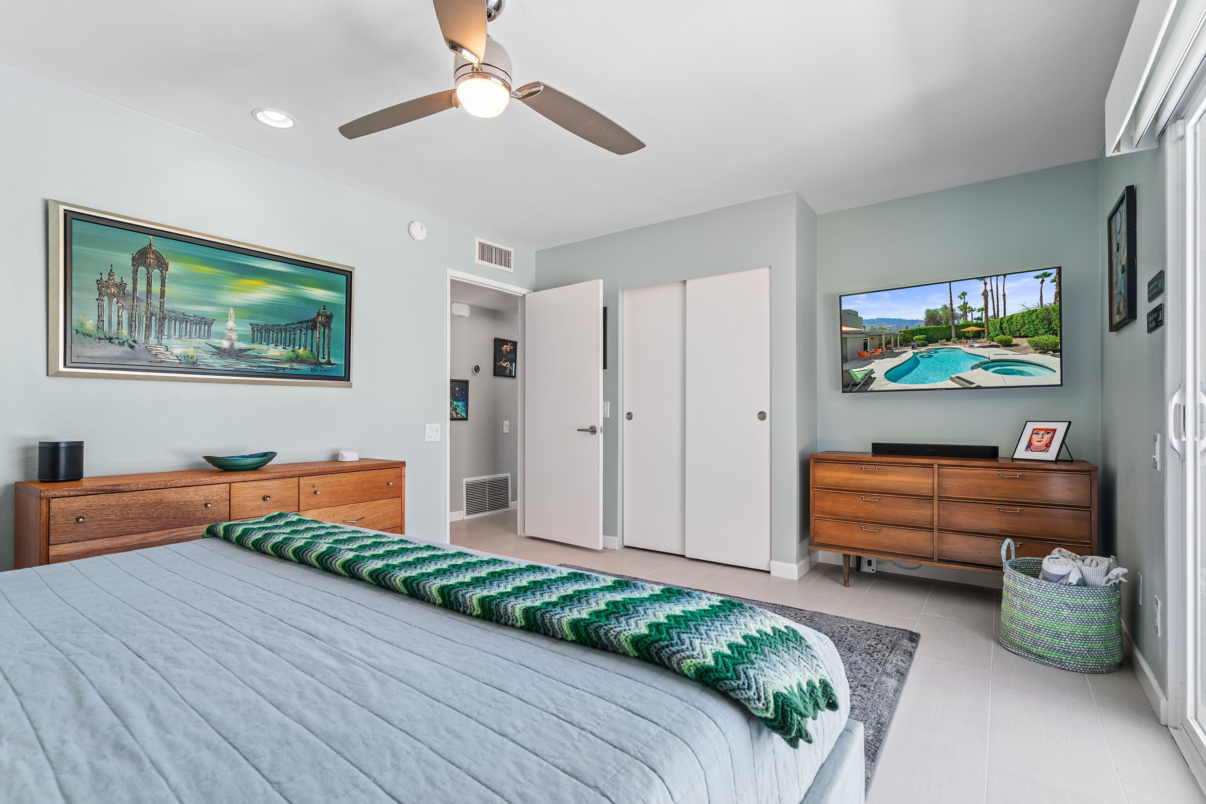 Ein Schlafzimmer mit Bett, Deckenventilator, Gemälde, Fernseher und Kleiderschrank.