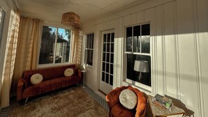 Ein Zimmer mit einem roten Sofa, einem braunen Sessel, einem kleinen Tisch mit einer Lampe und einem großen Fenster mit Vorhängen.