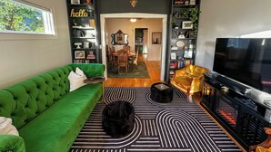 Ein Wohnzimmer mit einem grünen Sofa, einem schwarz-weißen Teppich, einem Fernseher und einem Bücherregal.