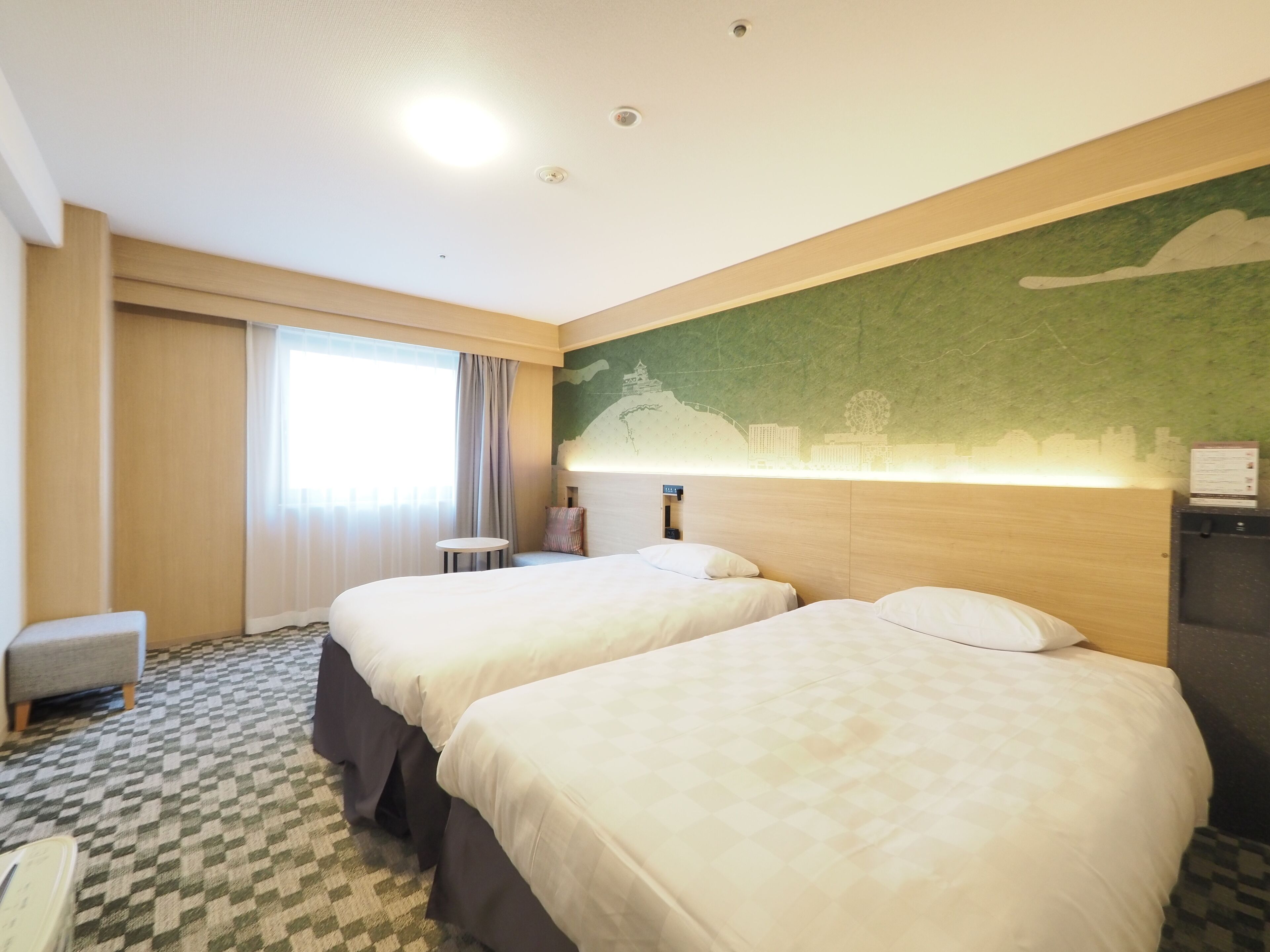A hotel room with two beds, a small table, a chair, and a wall mural.