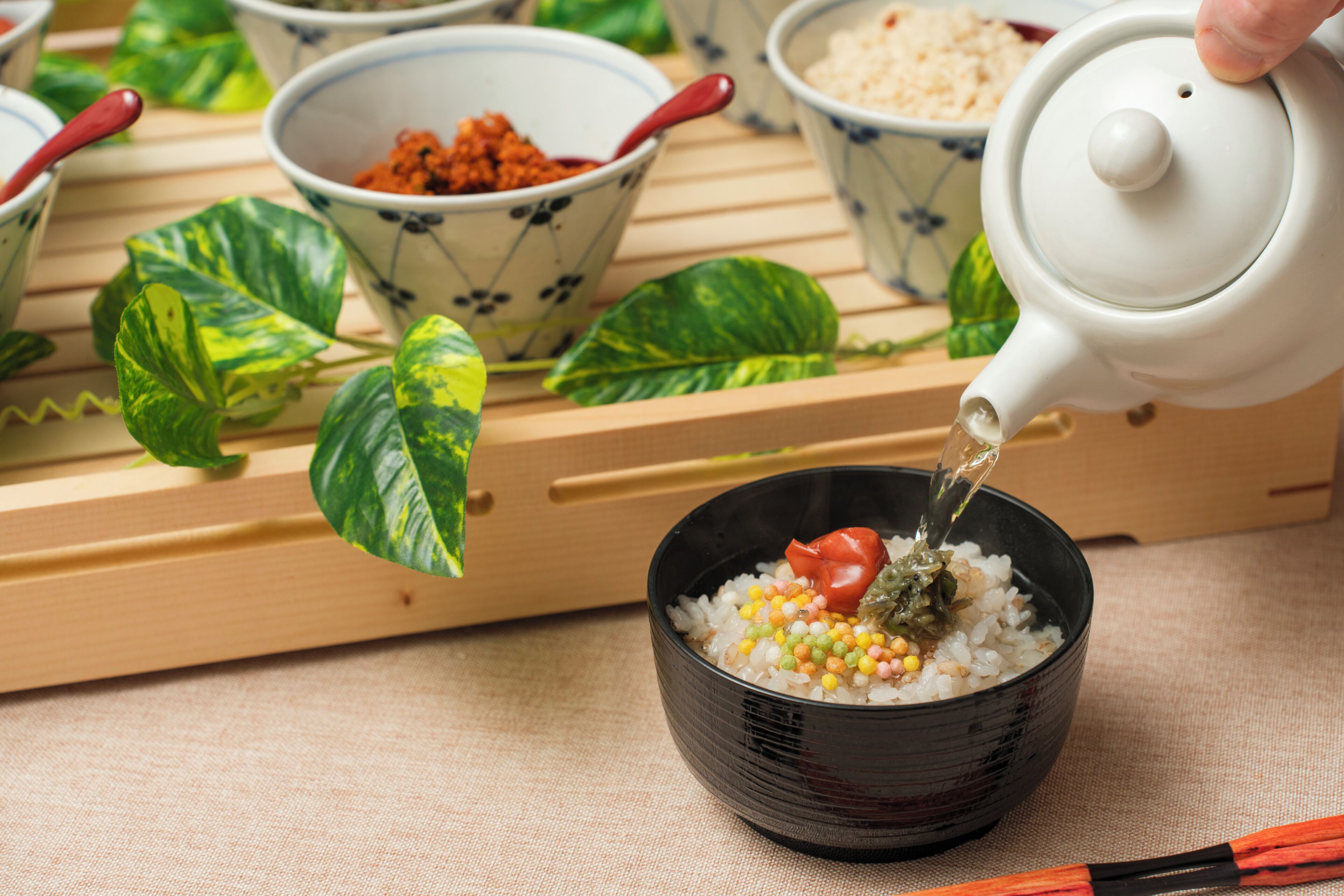 A teapot pouring tea into a bowl of rice with vegetables.