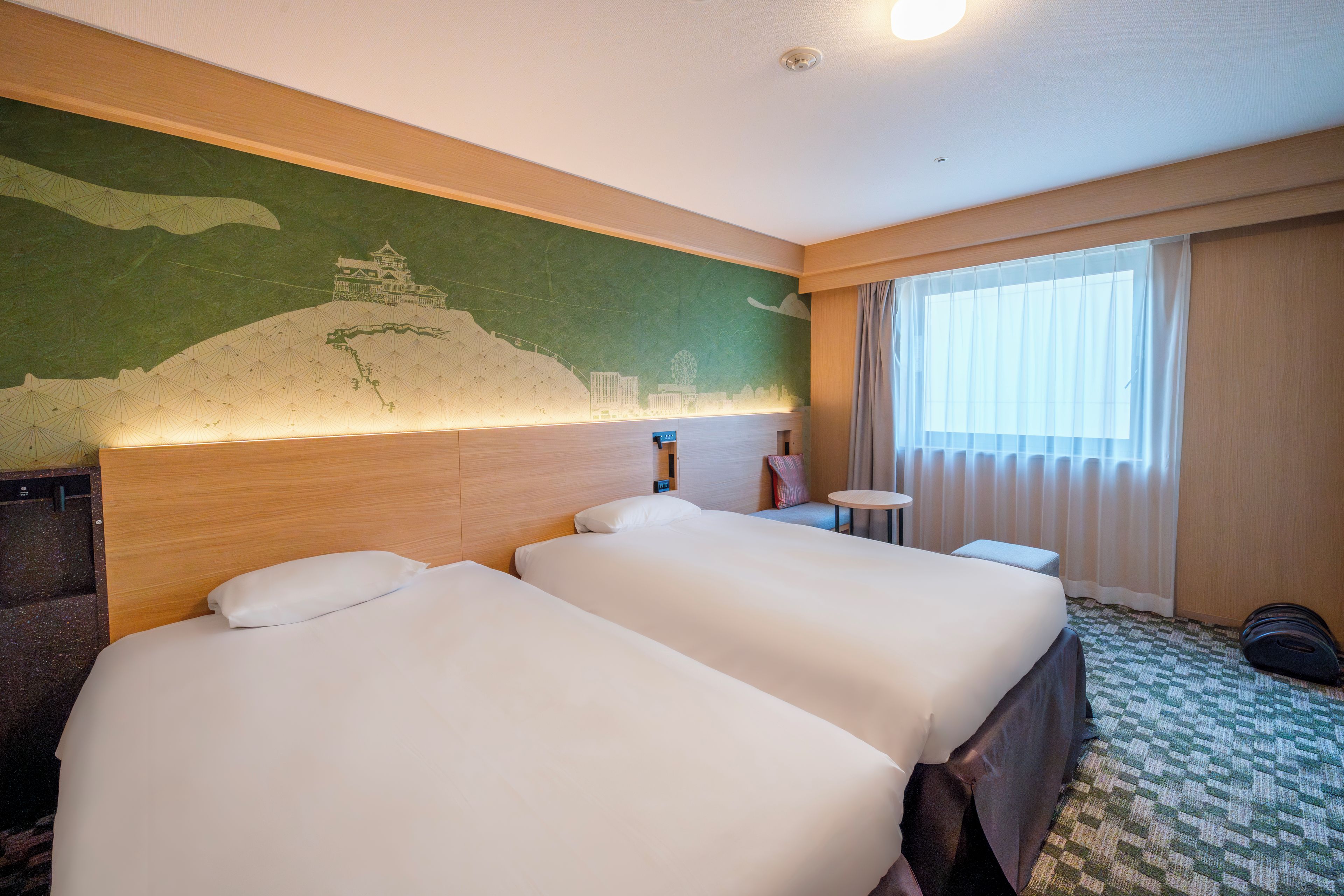 A hotel room with two beds, a cityscape mural on the wall, a round table, and a window with curtains.
