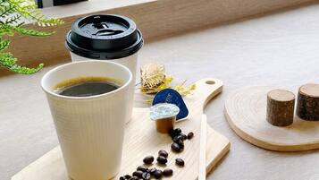 A cup of coffee on a wooden tray with coffee beans, a spoon, and a small container of creamer.