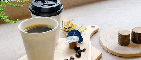 A cup of coffee on a wooden tray with coffee beans, a spoon, and a small container of creamer.