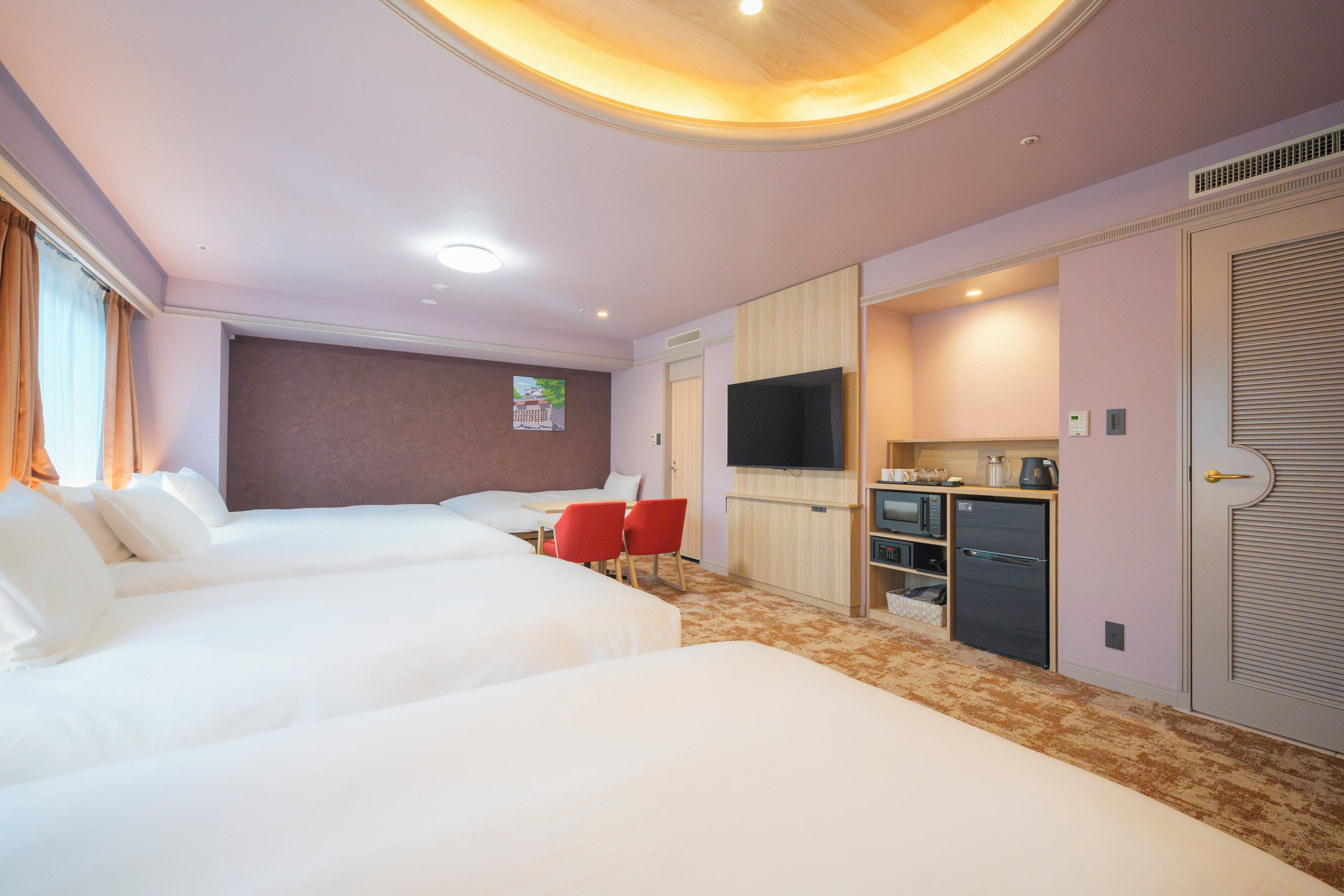 Habitación de hotel con dos camas, un televisor, un rincón americano y una silla roja.