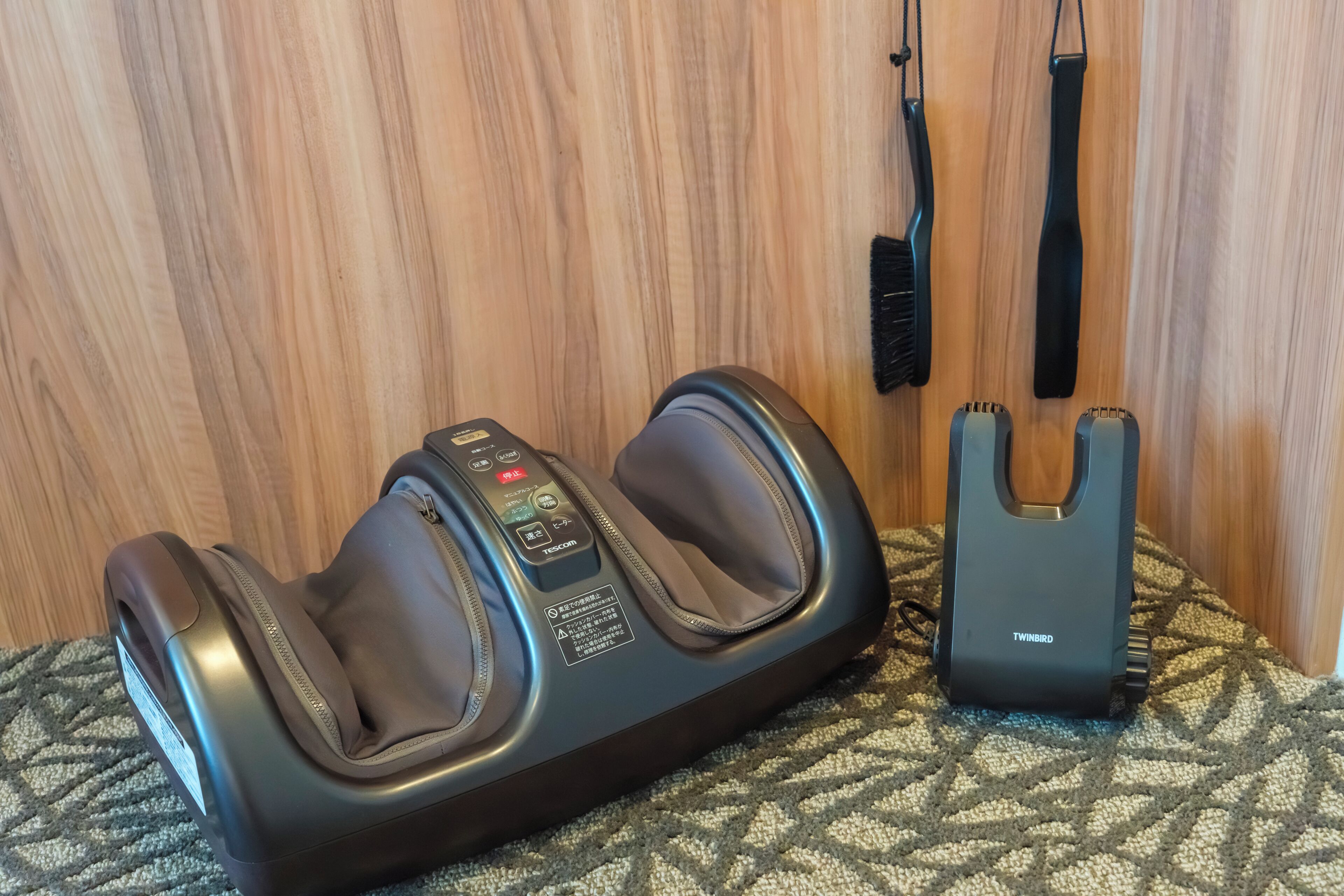 A massage chair with a control panel and a remote control on a patterned carpet.