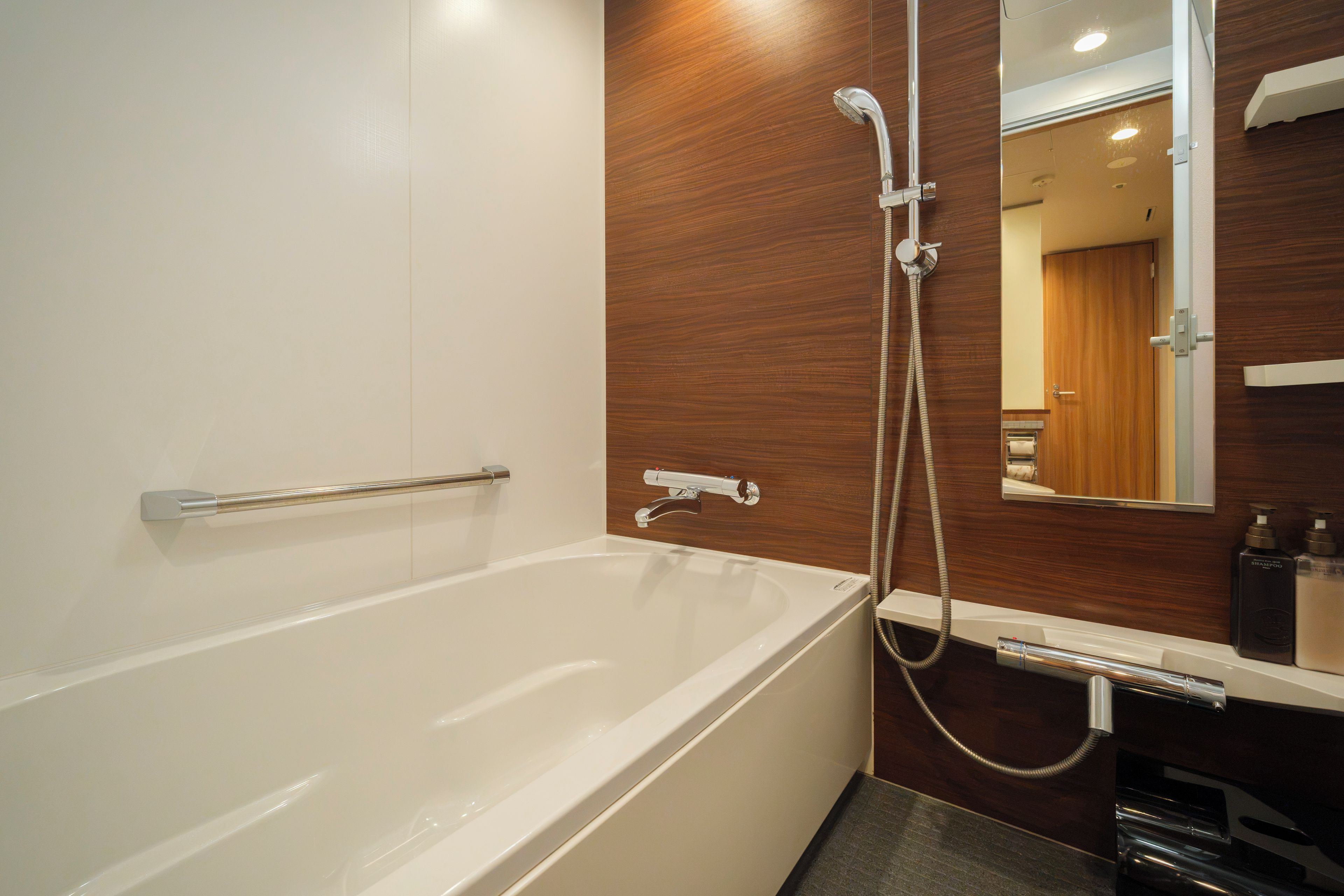 A modern bathroom with a white bathtub, wooden panel wall, and a mirror above the sink.