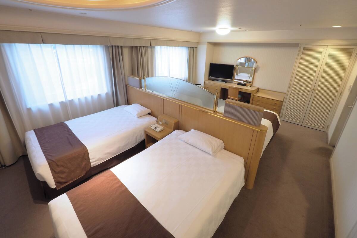 A hotel room with two beds, a desk with a computer, a TV, and a mirror.