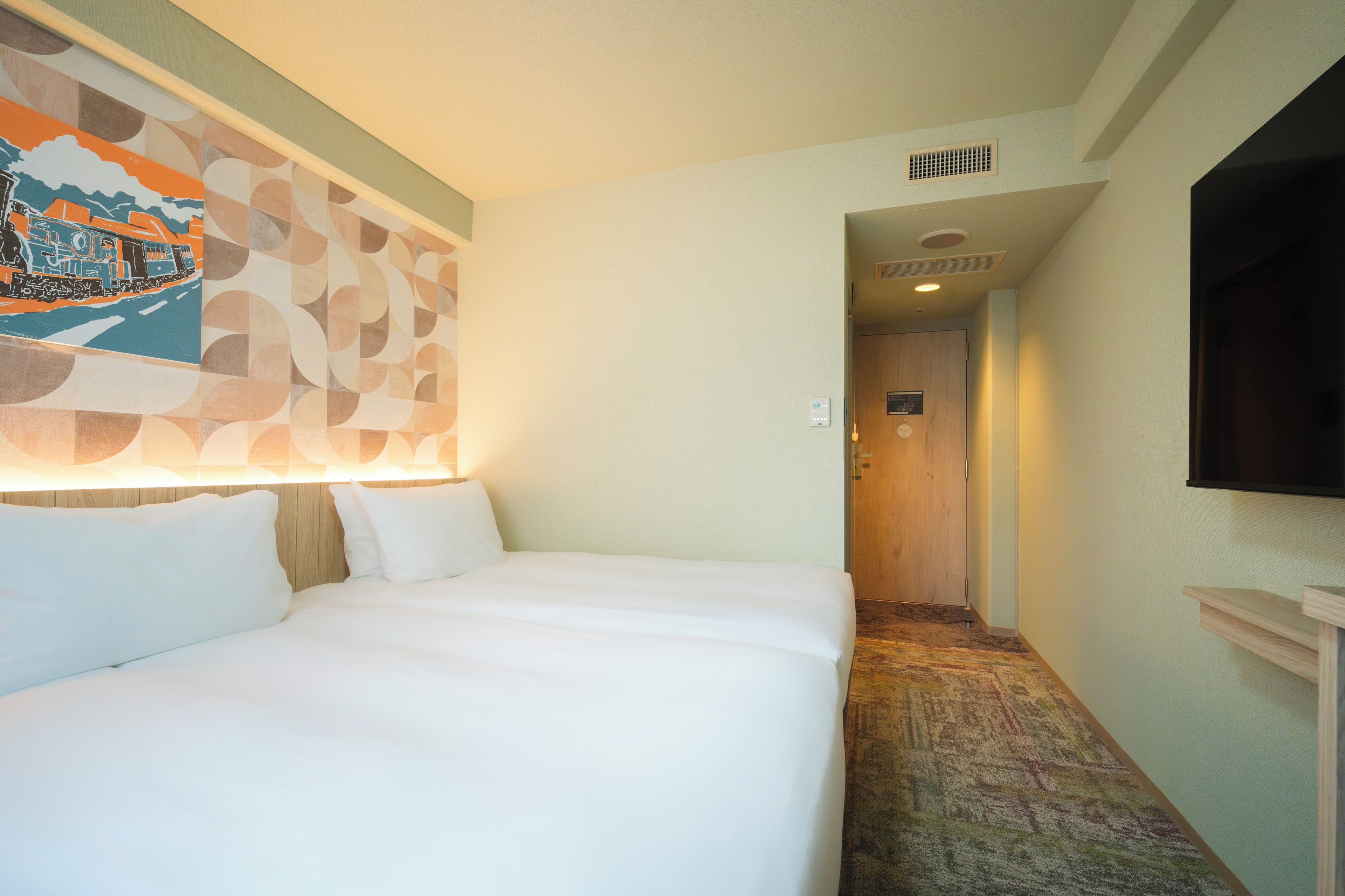 Ein Hotelzimmer mit einem Bett, einem an der Wand befestigten Fernseher und einem Flur, der zu einem anderen Raum führt.