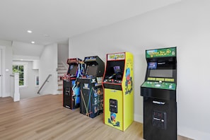 Une pièce avec un plancher en bois, des murs blancs et trois bornes d’arcade.