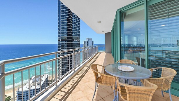 A balcony with a view of the ocean and a tall building. There is a table with chairs and a glass door. - Panoramic Ocean View Sub-Penthouse 3mins to Beach (Surfers Paradise)