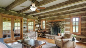 A log cabin interior with a stone fireplace, wooden furniture, and large windows. - Hummingbird's Rest - Wine Country Cabin Retreat (Dyke)