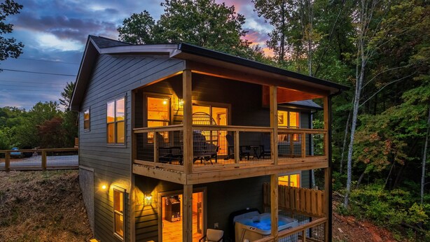 A two-story wooden cabin with a balcony, a hot tub, and a covered outdoor seating area.