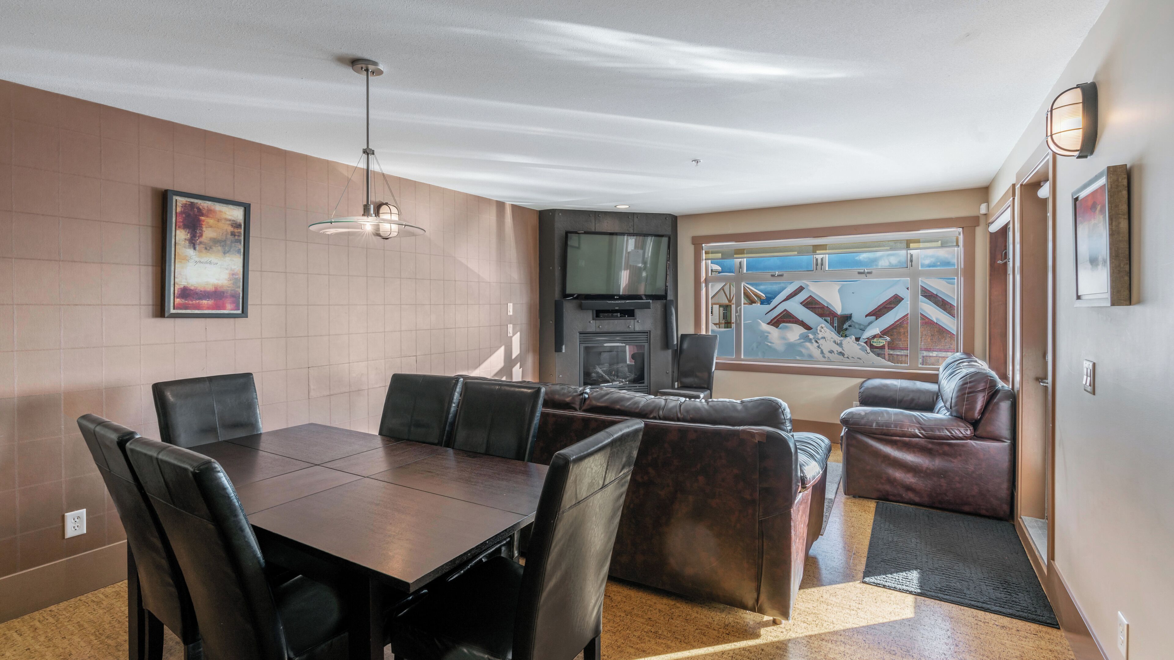A modern living room with a dining area, a fireplace, and a large window with a snowy view.