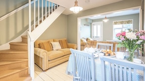 Una sala de estar con una escalera, un comedor con una mesa preparada para el desayuno, y una cocina al fondo.