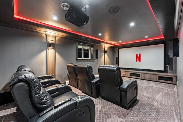A home theater room with leather reclining chairs, a large screen, and red ambient lighting.