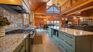 A spacious kitchen with granite countertops, a central island, and a dining area with a high ceiling and wooden beams.
