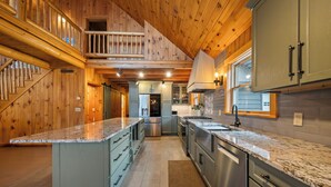 A spacious kitchen with wooden paneling, a central island, stainless steel appliances, and a view to the living area.